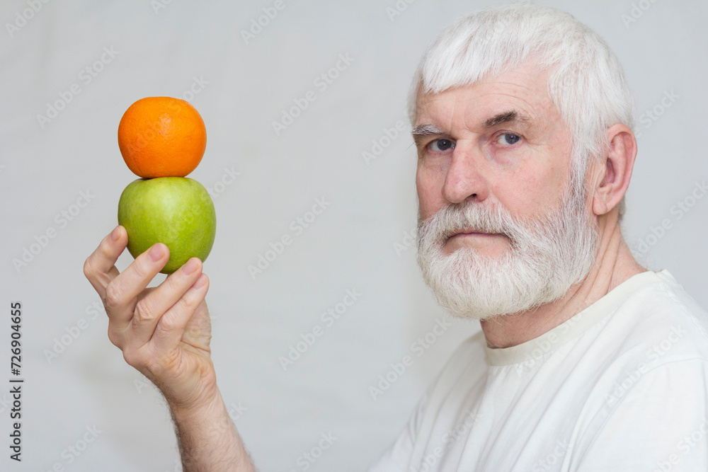 A gray-haired elderly man holds a tangerine and a green apple in his hands A gray-haired elderly man holds a tangerine and a green apple in his hands