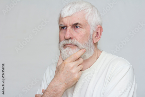 handsome elderly man with a gray beard holds his beard with his hands