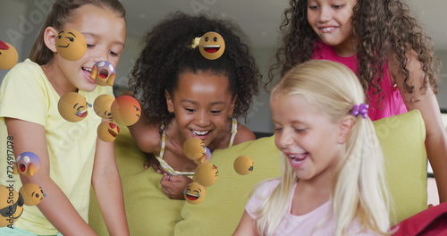 Image of various emojis moving over happy diverse schoolgirls using tablet together at beak time