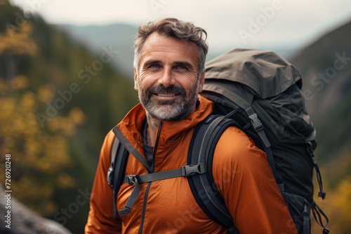 Handsome bearded man is hiking in the mountains. He is looking at camera and smiling.