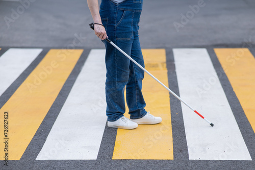 Close-up of the legs of a blind woman crossing the road at a crosswalk with a cane. 