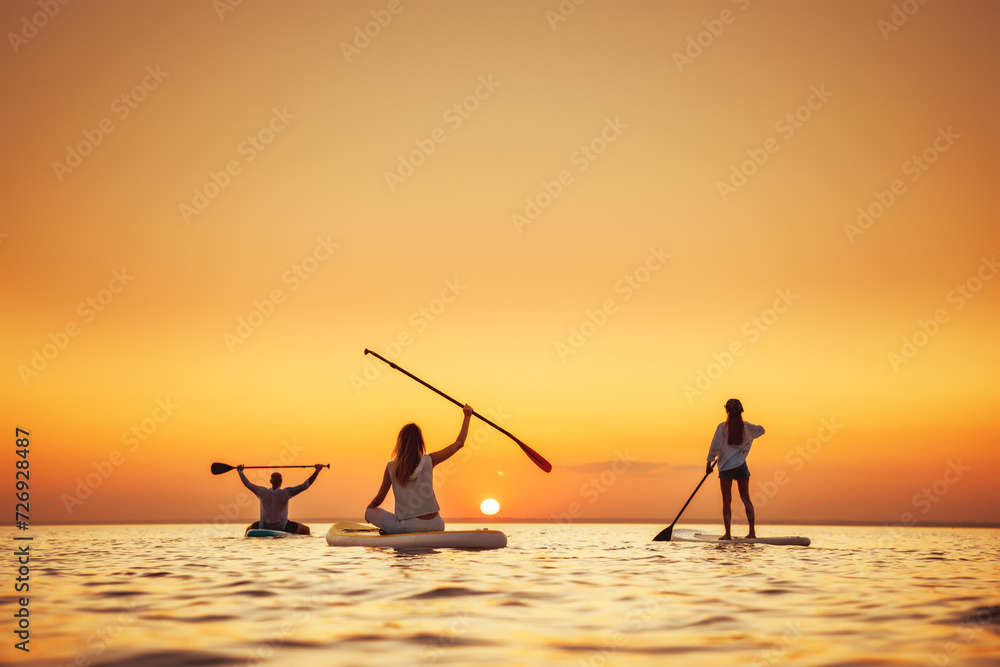 Fototapeta premium Group of happy young friends are relaxing with stand up paddle sup boards at calm sunset lake