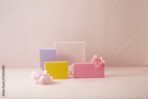 A pink and yellow  light purple square podium against light pink background. With flower. An empty platform for display cosmetic products  food and props.