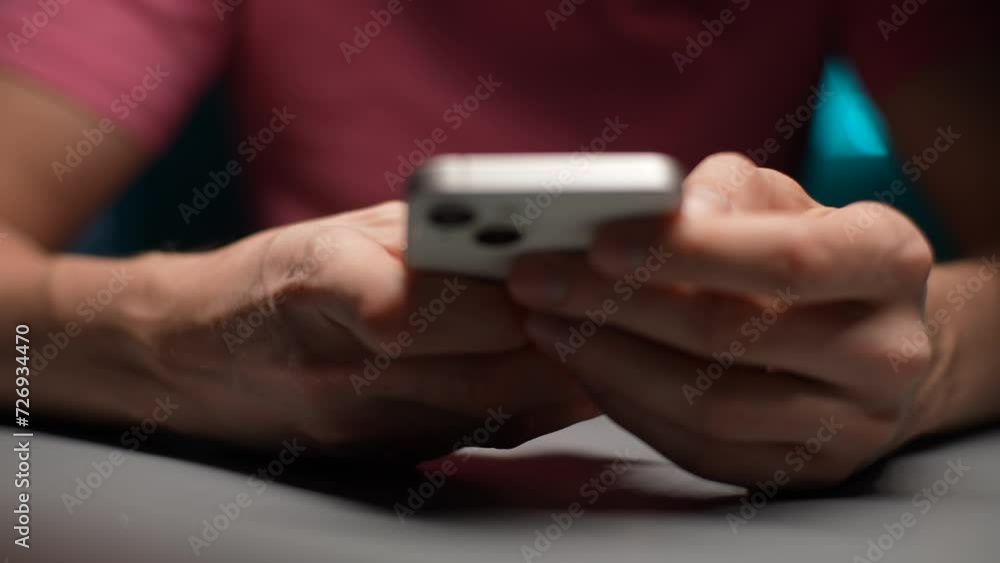 Extreme close-up of unrecognizable businessman student worker sitting at desk holding mobile phone in hands texting message in web chat surfing corporate network reading news in dark room, slowmo. Extreme close-up of unrecognizable businessman student worker sitting at desk holding mobile phone in hands texting message in web chat surfing corporate network reading news in dark room, slowmo.