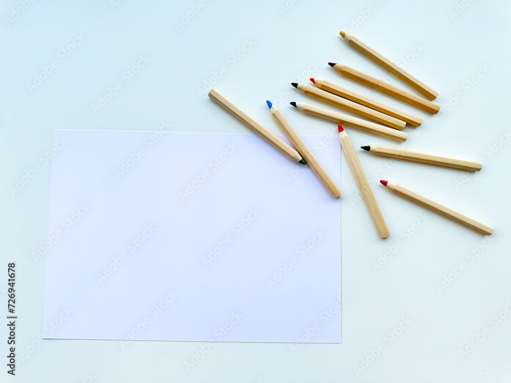 Colored pencils on table, on paper, on white background. Top view. Colored pencils on table, on paper, on white background. Top view.