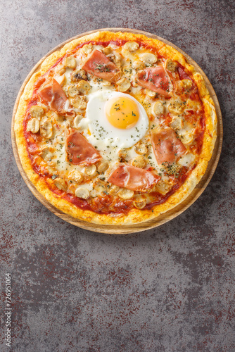 Italian Pizza Bismarck topped with tomato sauce, melted cheese, egg, mushrooms, ham close-up on a wooden board on the table. Vertical top view from above