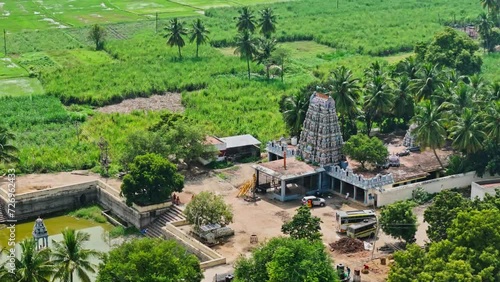 Rotating aerial side view of vintage Theni Temple with a pond in front and trees and greenery at background during sunny day in Theni, Tamil Nadu. photo