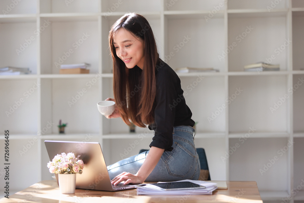 Smiling businesswoman working at her office desk, reading a newspaper and a book, surrounded by technology and creating a successful and professional workplace