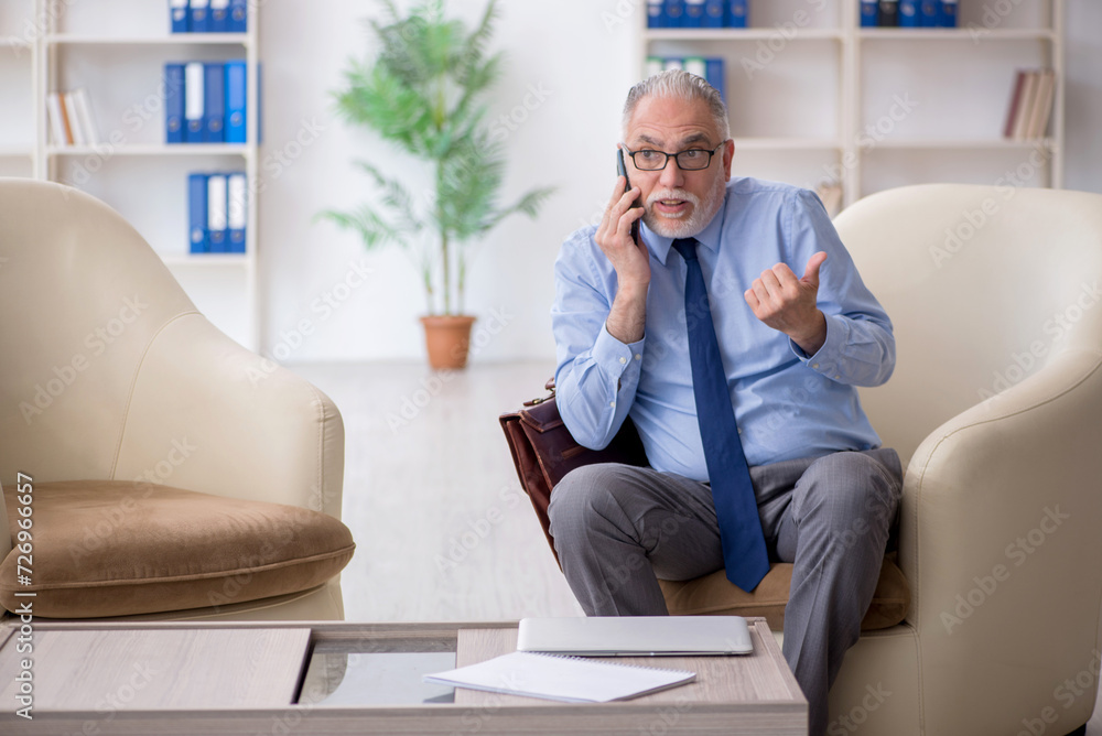 Fototapeta premium Old male employee speaking by phone at workplace