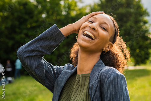 Photography Young African woman laughing with hand on head in a park, radiating joy and vivacity