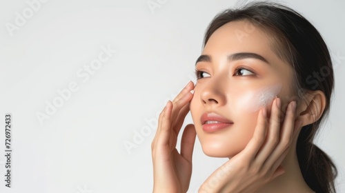 Elegant Asian woman gently applies facial moisturizer on her cheek