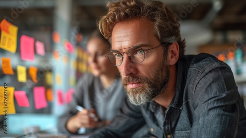 A focused man with glasses in front of colorful sticky notes on a wall, another person blurred., generative ai