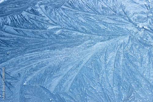 Frost flowers on a frozen flat surface in winter blue ice pattern background texture
