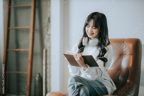 Portrait of a beautiful young Asian woman relaxing, holding a book, listening to music from headphones in Cafe, Asian girl smiles happily, relaxing on a vacation.