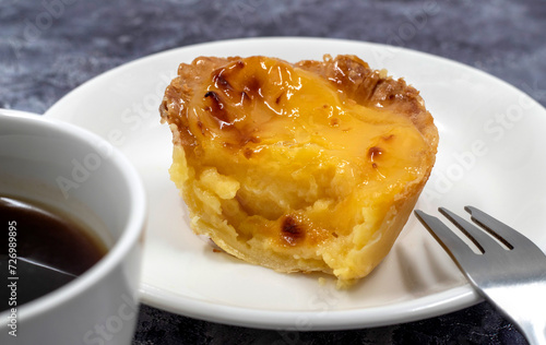 One uneaten Pastel de nata or Portuguese egg dessert on a white plate. Pastel de Belm is a small pie with a crispy puff pastry crust and a custard cream filling. Eating a small dessert, a cupcake. photo