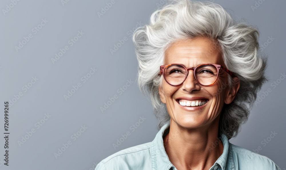 Confident and happy senior woman with stylish gray hair and glasses, smiling broadly, exuding positivity and experience on a light gray background