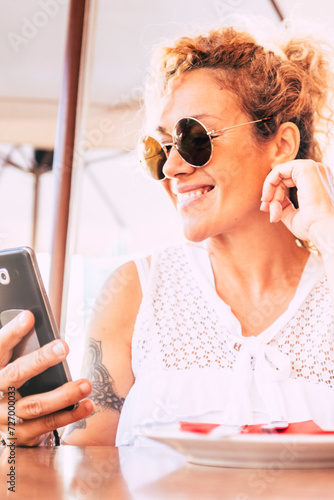 Beautiful and happy adult model woman use modern cellular phone at the restaurant with wifi connection - cheerful people and technology - modern lady with sunglasses photo