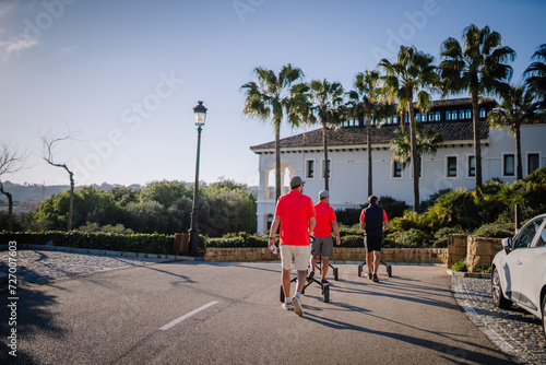 Fotografie Sotogrante, Spain - January 27, 2024 - Three golfers walking on a paved road towards a clubhouse surrounded by palm trees under a clear blue sky