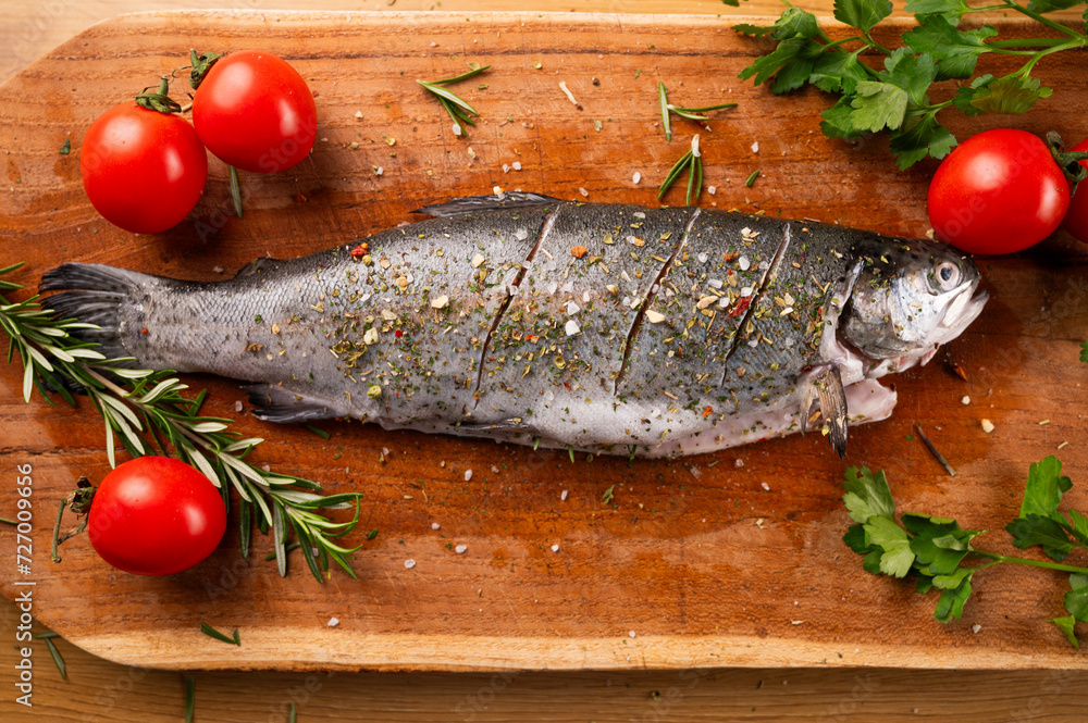 Fresh river trout with tomatoes and herbs de Provence on a kitchen wooden board. Cooking delicious and healthy food at home.Fresh fish trout and ingredients for cooking. Raw fish. Fresh river trout with tomatoes and herbs de Provence on a kitchen wooden board. Cooking delicious and healthy food at home.Fresh fish trout and ingredients for cooking. Raw fish.