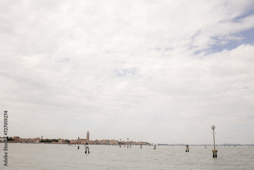 Venice, Italy - View of the Lagoon with City in Distance, Calm Water Surface with Wooden Poles