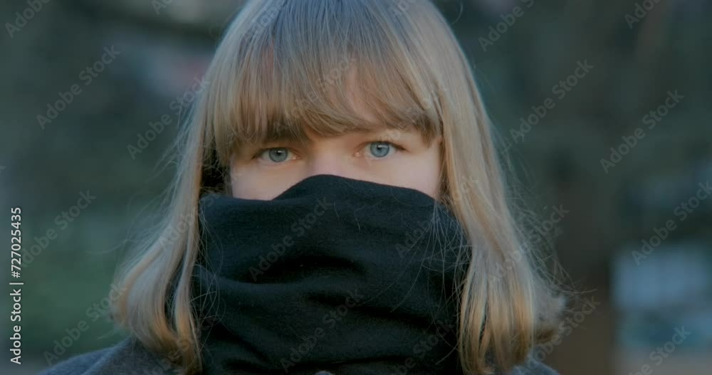 Closeup of a blonde woman with blue eyes looking in the camera with her face partially covered by a scarf. Closeup of a blonde woman with blue eyes looking in the camera with her face partially covered by a scarf.