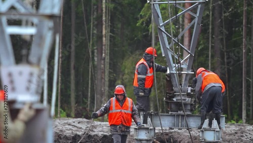 Workers are installing a power transmission tower in harsh conditions, erecting a communication tower.