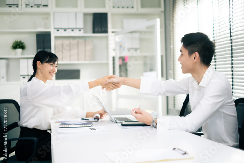 Businessman and Businesswoman sitting at desk, checking hand together in office after success dealing business with smile of happiness.