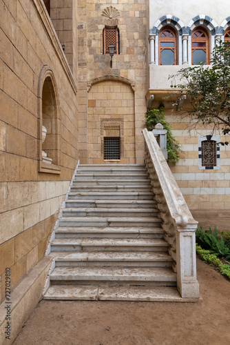 Marble staircase, leads up to a wrought iron window in a stone brick wall, framed by a decorative railing. The scene evokes a sense of mystery and history © Khaled El-Adawi