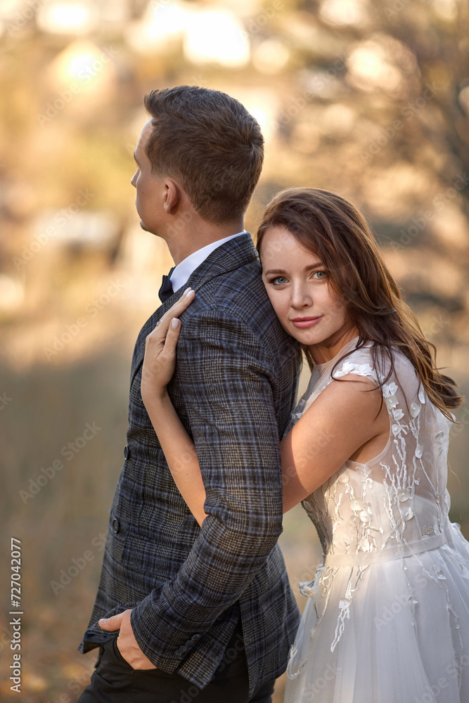 Naklejka premium beautiful sensual bride in white wedding dress and groom standing outdoor on natural background