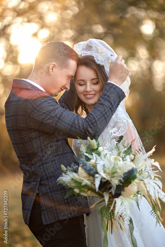 happy bride and groom enjoying romantic moments under veil outside on natural background in sunny day