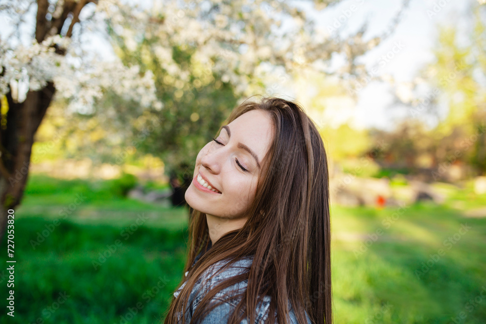 Portrait of a handsome smiling with teeth girl in a spring garden at sunset. A woman relaxes in a park with blooming apple and cherry trees. Portrait of a handsome smiling with teeth girl in a spring garden at sunset. A woman relaxes in a park with blooming apple and cherry trees.