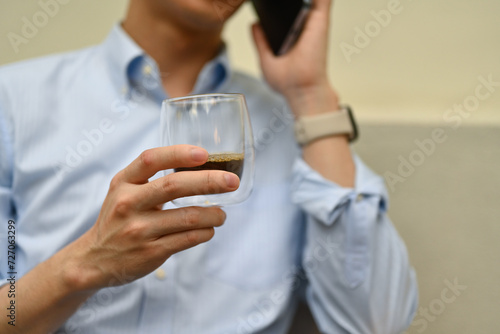 Close-up of an unrecognizable businessman business talking on the smartphone while sipping a coffee  Outdoor