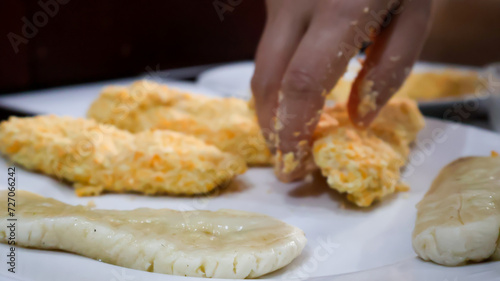 Close-up of a woman making fried banana by coating the banana in golden bread crumb to then be fried. Ideal for food blogs, cooking concepts, food enthusiasts, and cooking-themed designs. 