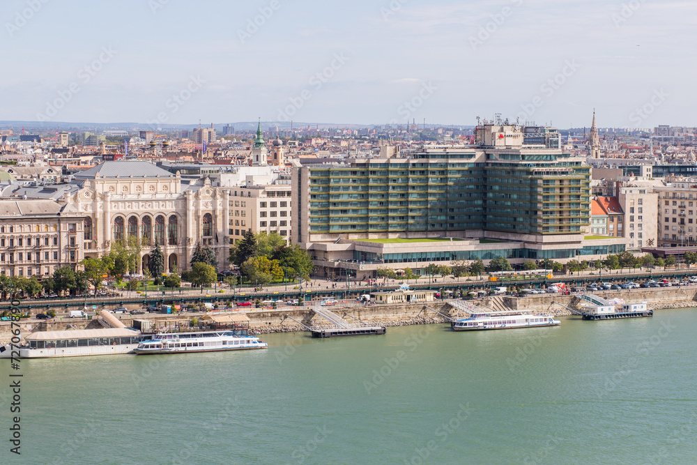 Embankment with several ships and boats. Clear blue water of the river. Modern buildings in a big city. Architecture with columns and glass facade.