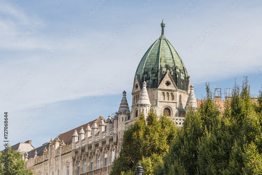 Beautiful roof of a building with a green dome. Gothic in the exterior. View of the top of the building through the green trees. Landmark of Budapest.