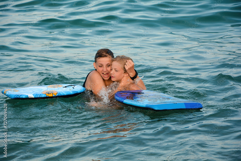 Two children have fun in the water, with swimming boards