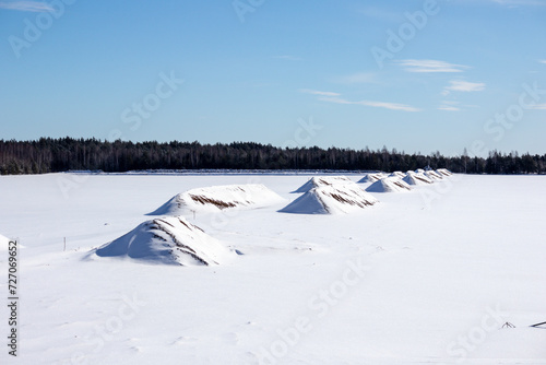 Peat field in winter with several peat hills covered with snow against the background of trees and blue sky