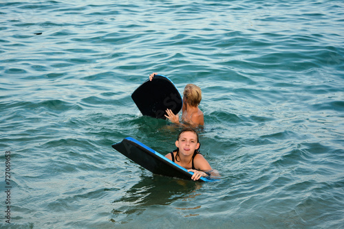 Two children with a swimming board in the water, girl cheekily sticks out her tongue photo