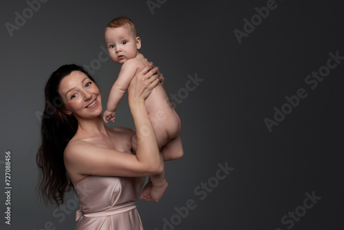 a beautiful young woman with long dark hair in a light dress holds a little boy in her arms. happy mother hugging her son on a dark background with space for text