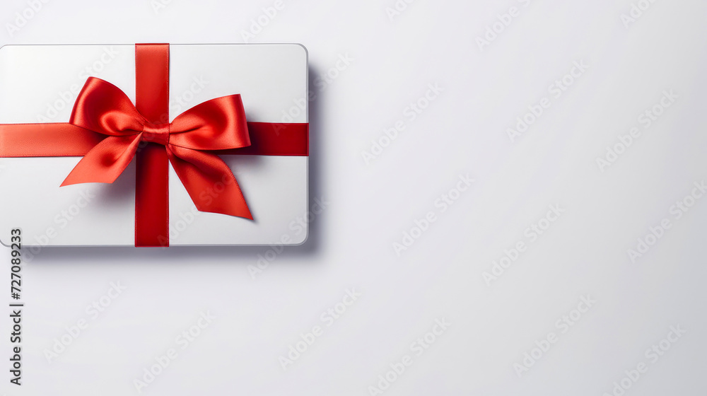 Blank white gift card with a red ribbon bow on a grey background with minimal shadow and conceptual design. Copy space. Blank white gift card with a red ribbon bow on a grey background with minimal shadow and conceptual design. Copy space.