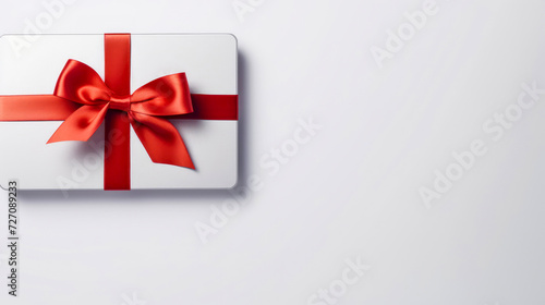 Blank white gift card with a red ribbon bow on a grey background with minimal shadow and conceptual design. Copy space.