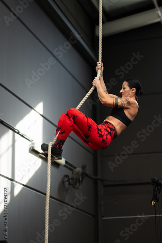 Strong woman climbing a rope in a cross training gym