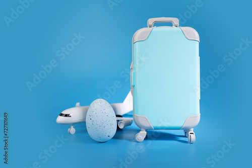 Flight booking concept, Easter egg and airplane with suitcase on blue, holiday journey