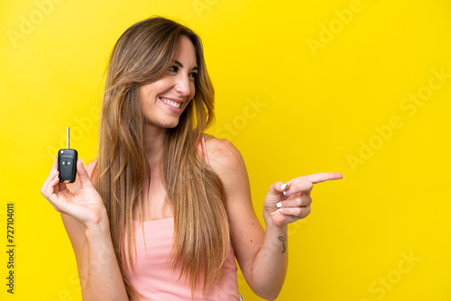 Young caucasian woman holding car keys isolated on yellow background pointing to the side to present a product