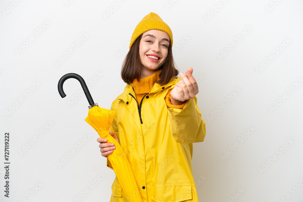 Young Ukrainian woman with rainproof coat and umbrella isolated on white background making money gesture Young Ukrainian woman with rainproof coat and umbrella isolated on white background making money gesture