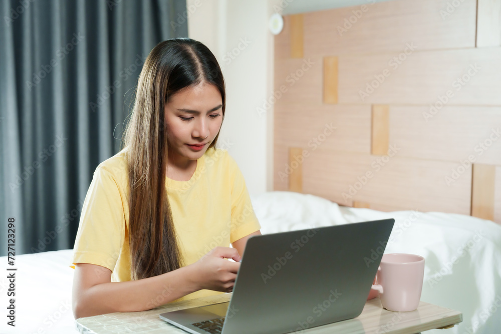 Young woman in yellow shirt focuses intently on her laptop, immersed in her work in a cozy bedroom. Engaged in her task, female analyzes content on her laptop, signifying diligent remote work Young woman in yellow shirt focuses intently on her laptop, immersed in her work in a cozy bedroom. Engaged in her task, female analyzes content on her laptop, signifying diligent remote work