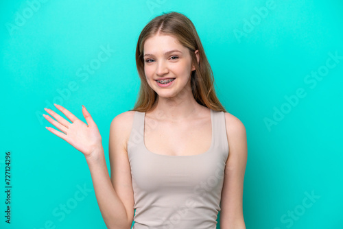 Teenager Russian girl isolated on blue background saluting with hand with happy expression