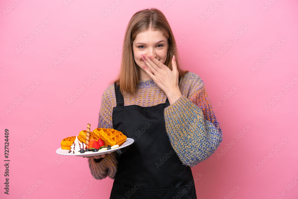 Teenager Russian girl holding a waffles isolated on pink background happy and smiling covering mouth with hand Teenager Russian girl holding a waffles isolated on pink background happy and smiling covering mouth with hand
