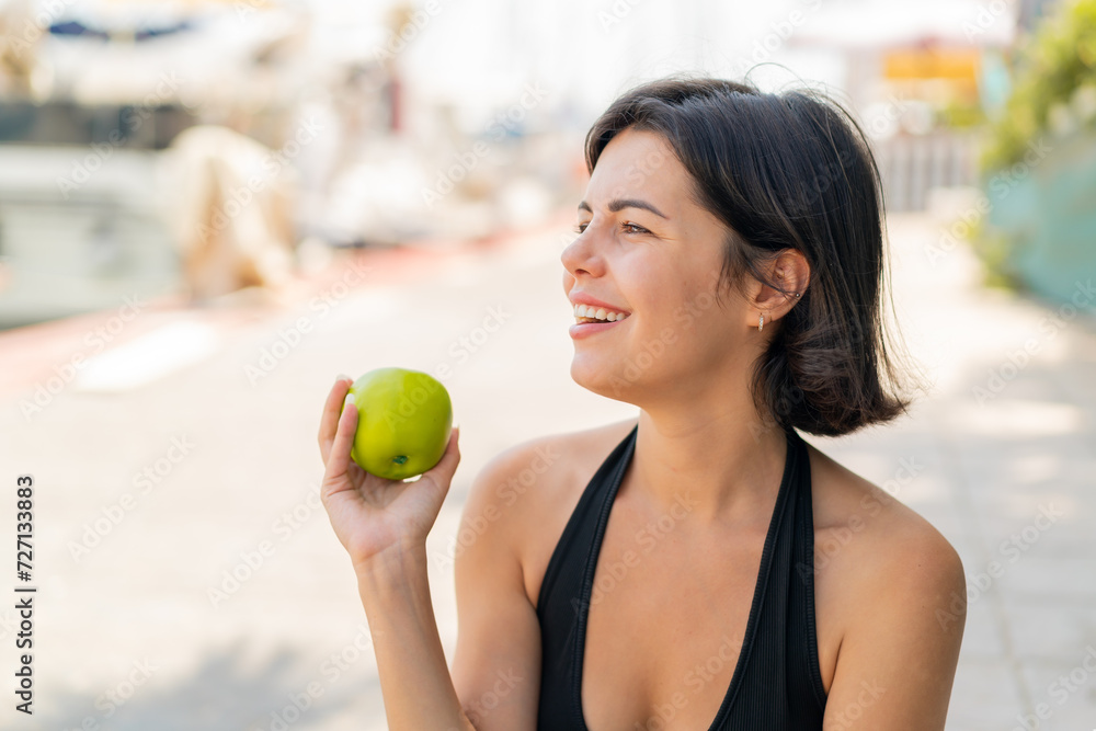 Young pretty Bulgarian woman at outdoors with an apple and happy Young pretty Bulgarian woman at outdoors with an apple and happy