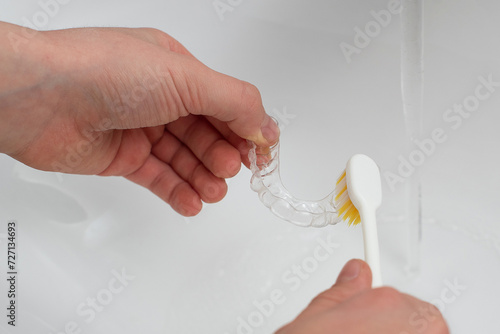 Hands clean aligners with a toothbrush under running water. Home care for aligners
